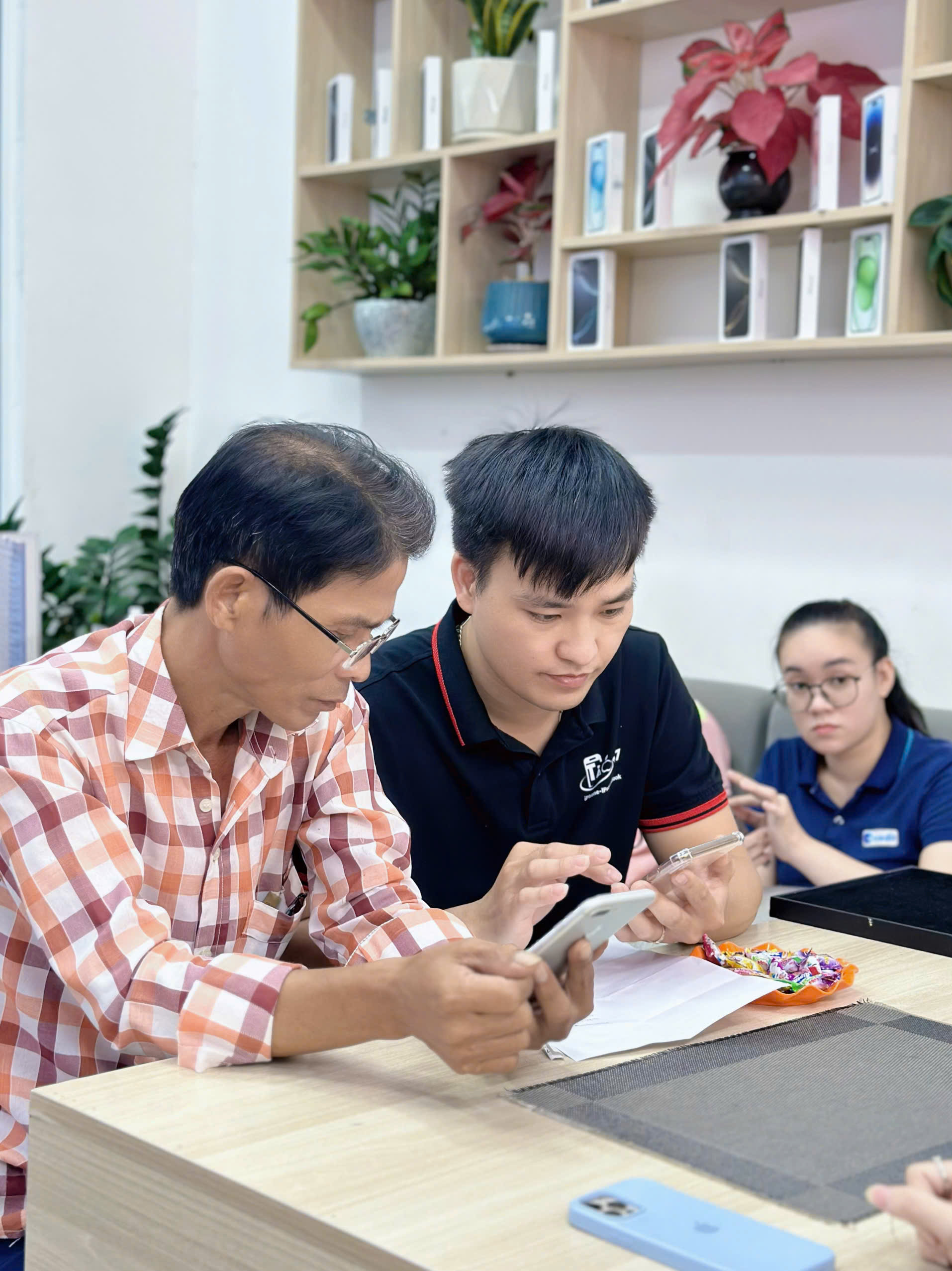 Nhân viên Táo 247 hỗ trợ khách lớn tuổi kiểm tra iPhone cũ tại cửa hàng Đà Nẵng