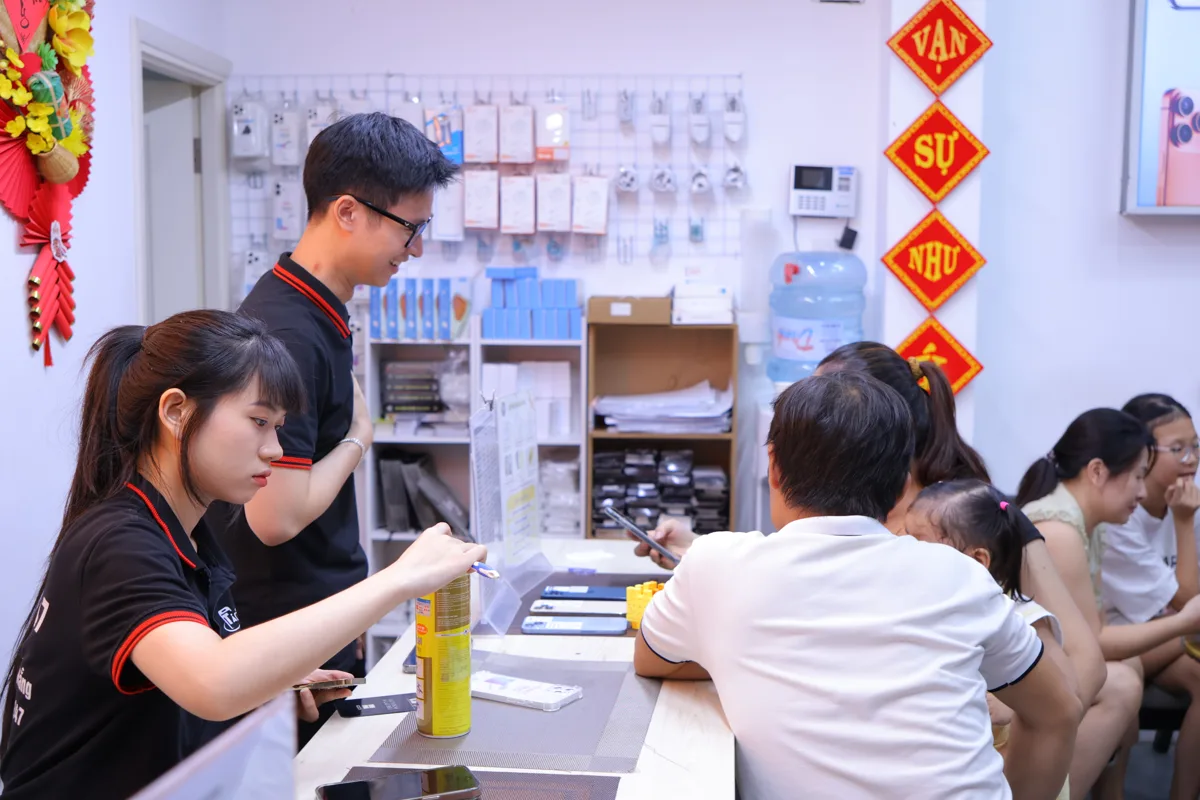 Nhân viên kỹ thuật Táo 247 xử lý máy tại quầy, khách ngồi chờ đối diện