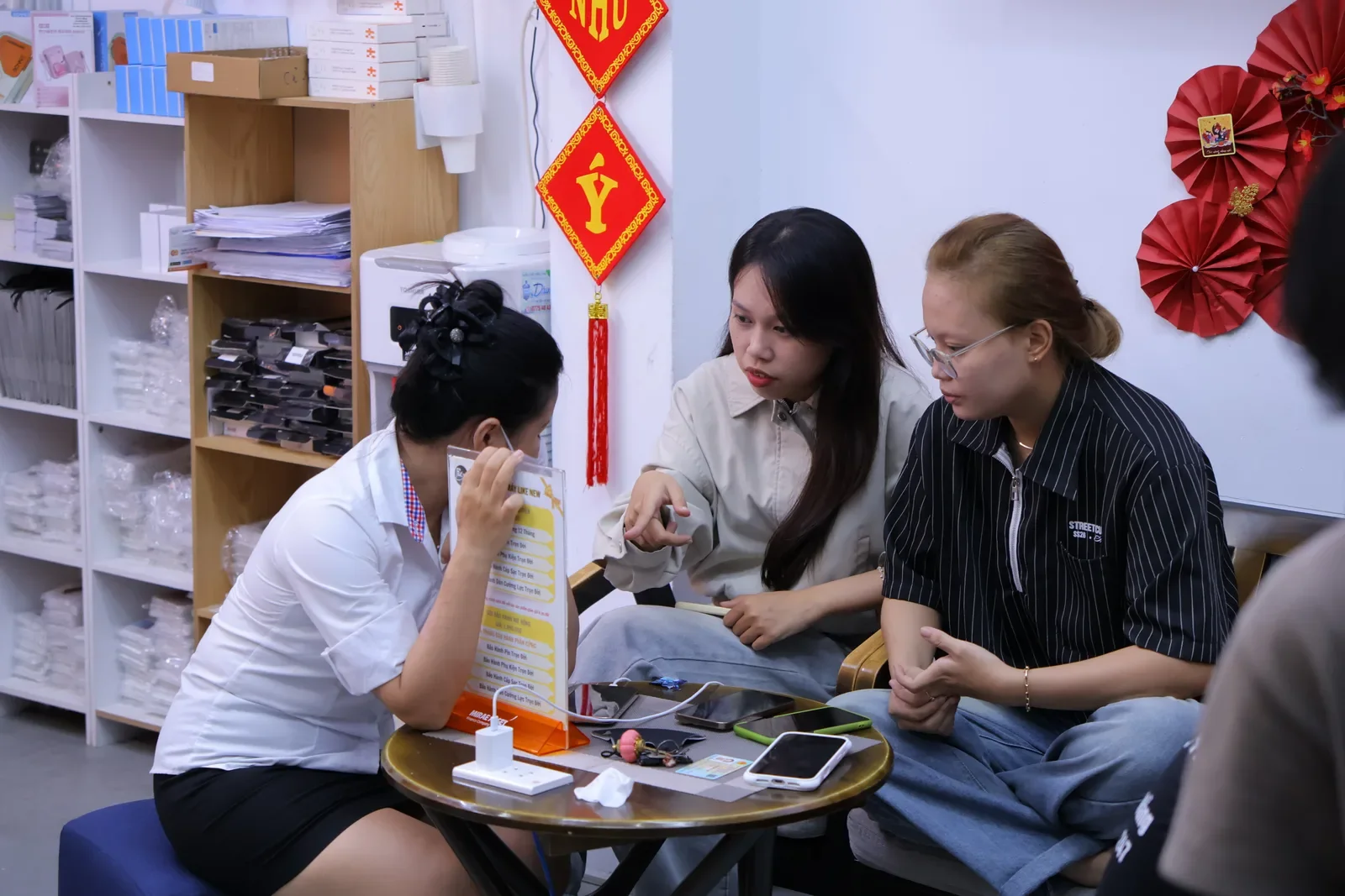 Nhân viên Táo 247 cầm bảng giá giải thích cho hai khách nữ tại khu ghế chờ