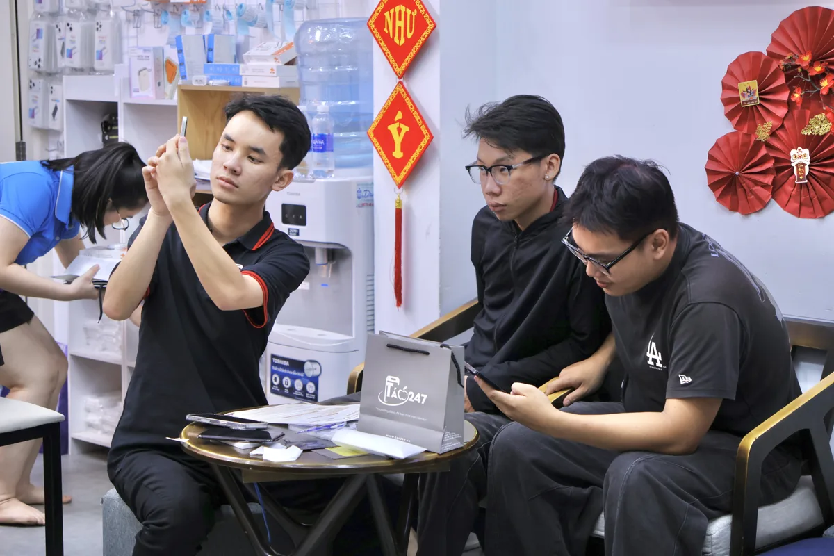 Nhân viên Táo 247 soi màn hình iPhone trước mặt hai khách